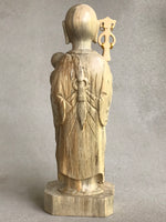 Load image into Gallery viewer, JIzo man standing, holding a staff and a baby, 25cm, 10 inches, color variation in wood from warm light brown to grey grain. back view.
