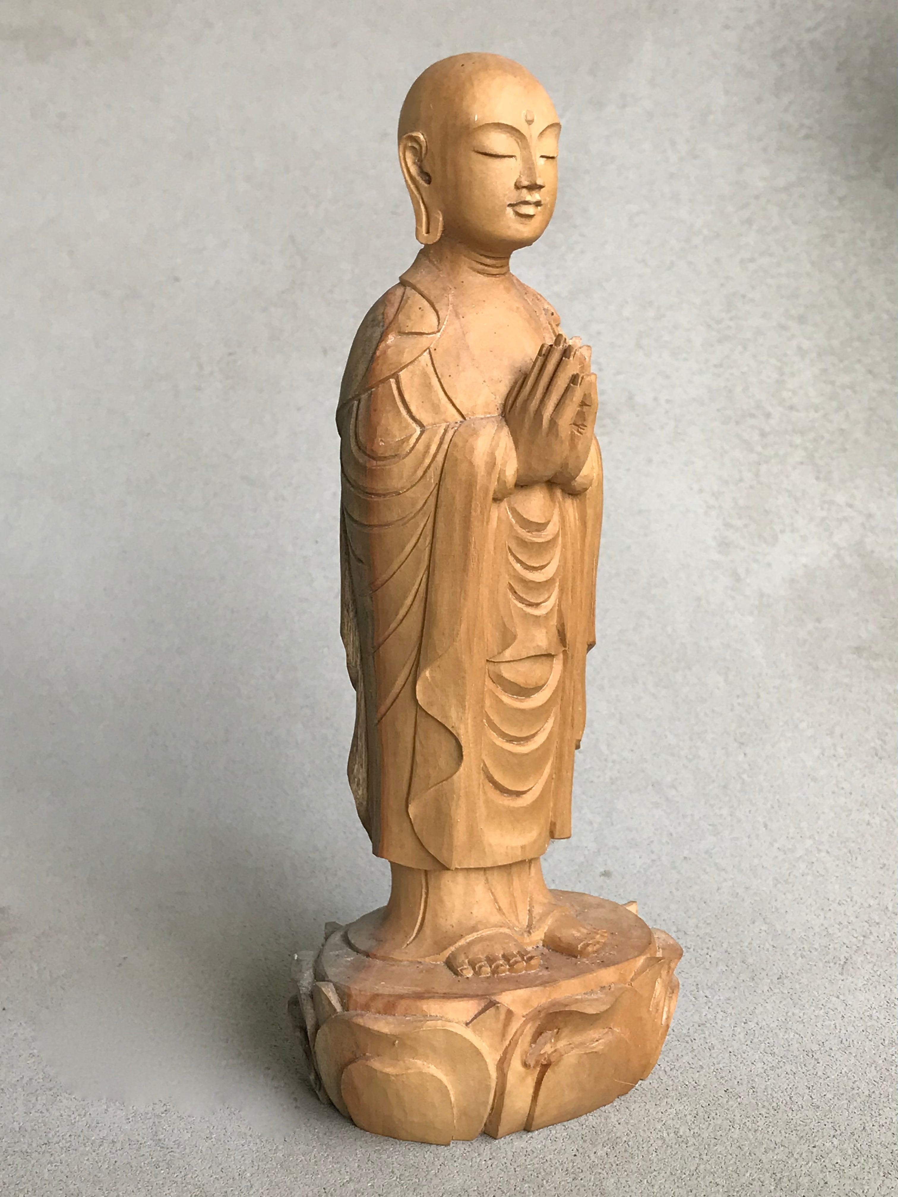 Hand carved wood statue of Jizo man with his palms together, standing on a lotus. 3/4 view