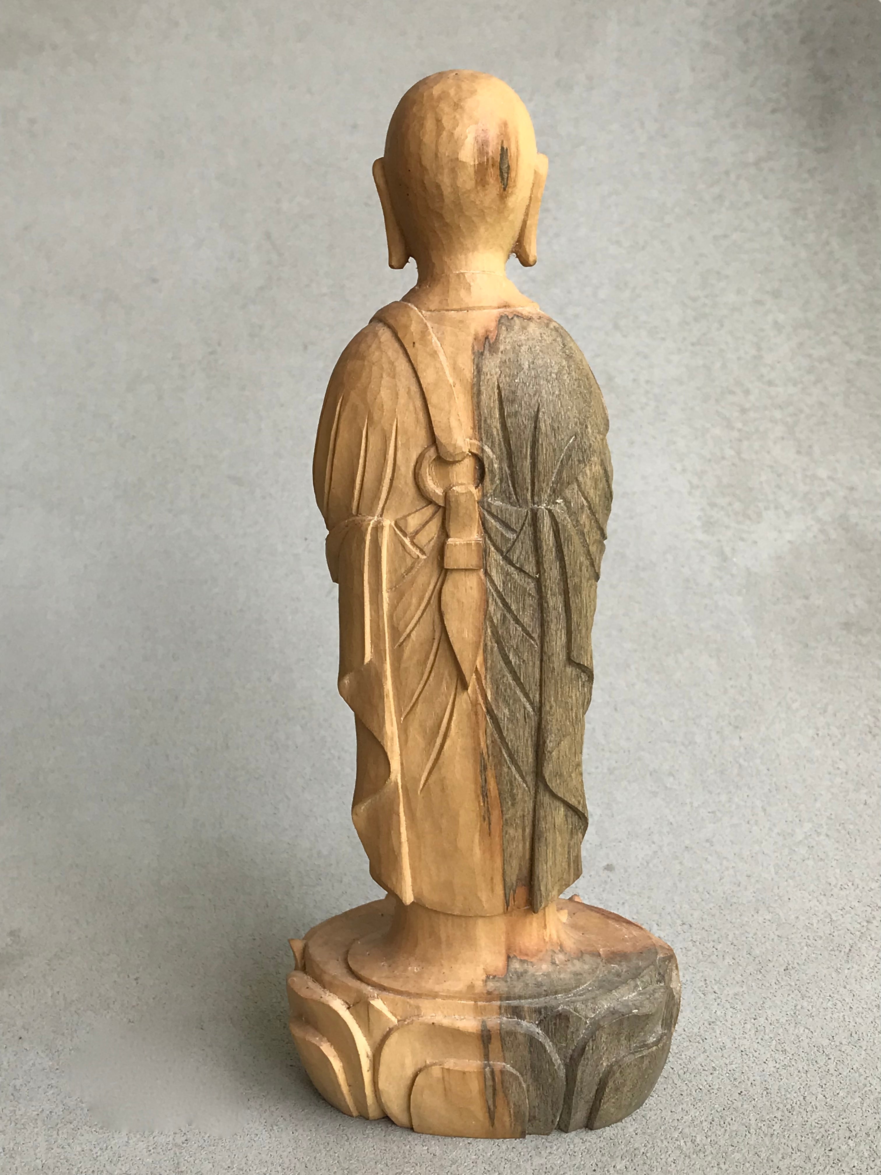 Hand carved wood statue of Jizo man with his palms together, standing on a lotus. Back view. wood color goes from warm brown to grey