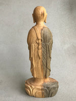 Load image into Gallery viewer, Hand carved wood statue of Jizo man with his palms together, standing on a lotus. Back view. wood color goes from warm brown to grey
