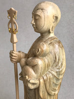 Load image into Gallery viewer, JIzo man standing, holding a staff and a baby, 25cm, 10 inches, color variation in wood from warm light brown to grey grain. close up view of left side

