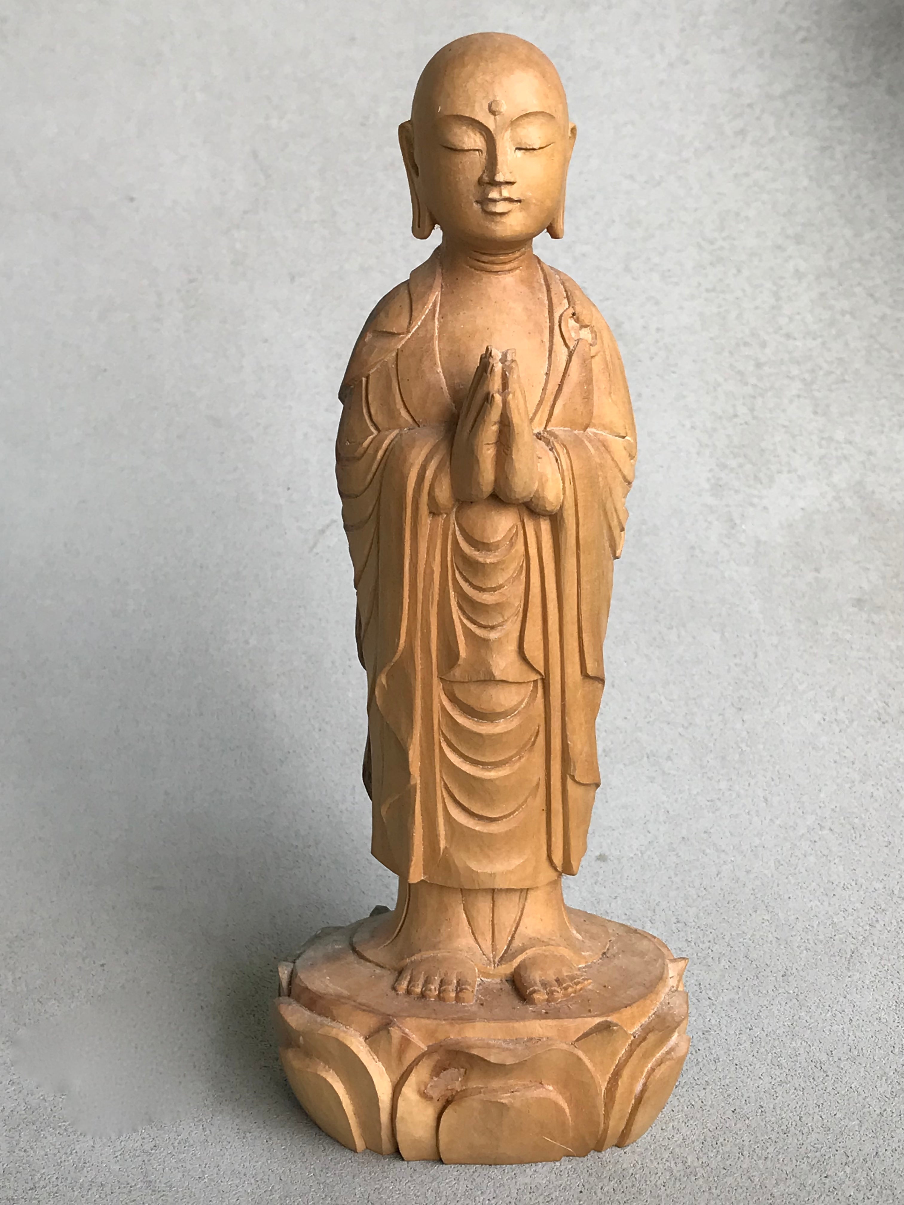 Hand carved wood statue of Jizo man with his palms together, standing on a lotus. 