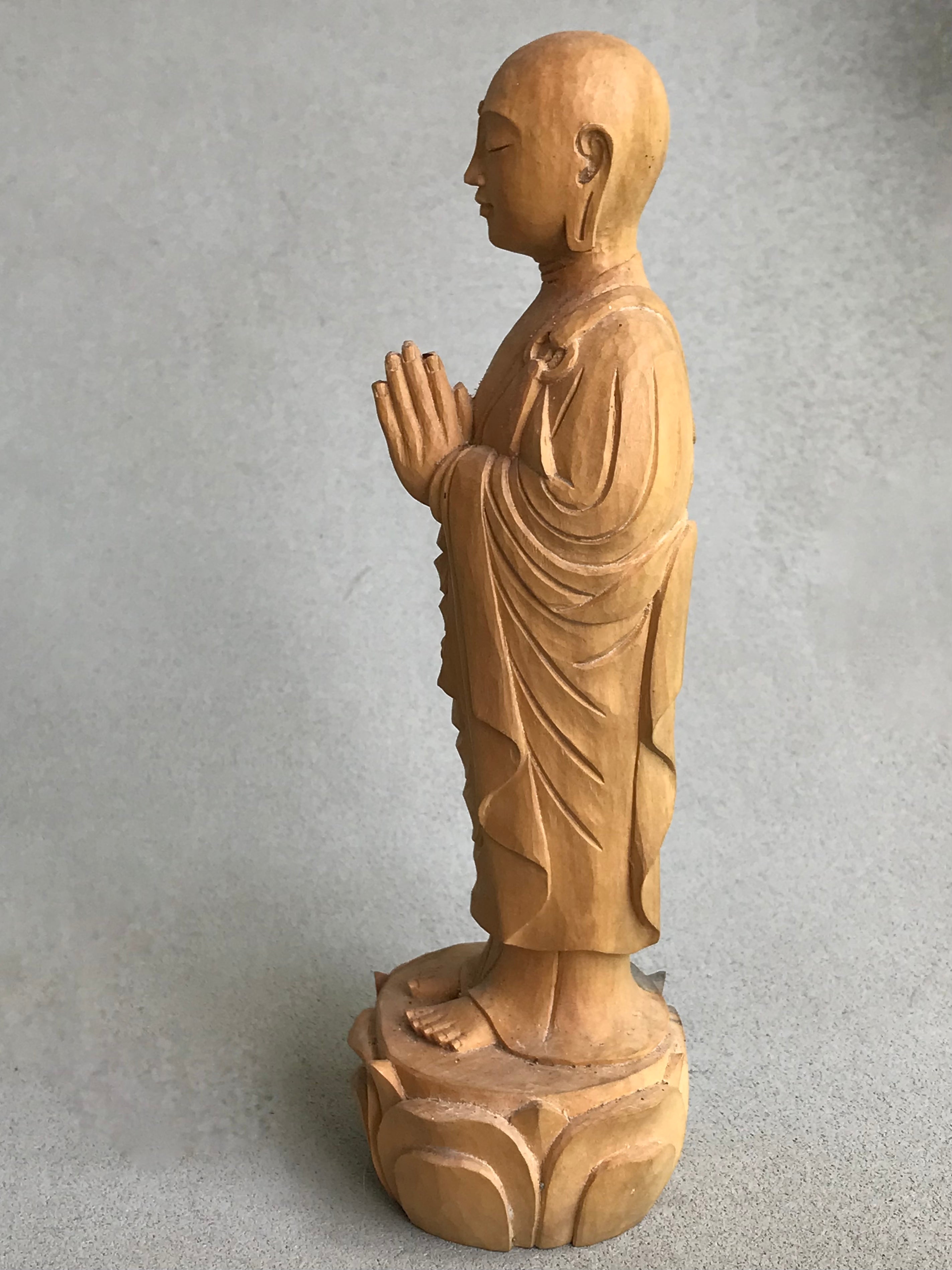 Hand carved wood statue of Jizo man with his palms together, standing on a lotus. Side view