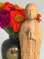 Load image into Gallery viewer, Hand carved wood statue of Jizo man with his palms together, standing on a lotus. Close up with flowers
