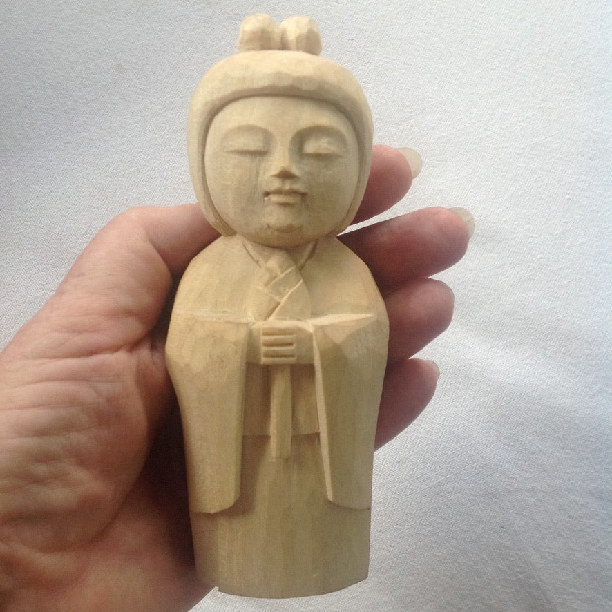 5 inch tall light colored wood hand carved statue of a Japanese Kuan Yin, knows as Kannon, holding a lotus.