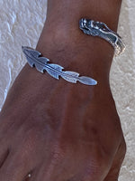 Load image into Gallery viewer, A close-up of a person's wrist wearing  silver-toned  2 ended dragon bracelet. One end is a detailed feather-shaped tail and the other is the dragons head with long flowing horns.
