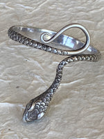 Load image into Gallery viewer, A silver snake-shaped cuff bracelet with detailed scales and a polished finish, displayed on a textured handmade cream colored paper background.
