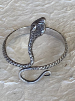Load image into Gallery viewer, A silver snake-shaped cuff bracelet with detailed scales and a polished finish, displayed on a textured handmade cream colored paper background. Head up
