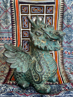 Load image into Gallery viewer, A detailed winged dragon figurine with a weathered green-bronze patina, posed in front of a colorful patterned textile backdrop.
