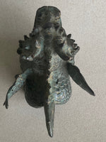 Load image into Gallery viewer, A dark bronze sculpture of a stylized creature or monster head with textured scales, spikes, and wing-like protrusions, photographed against a plain light beige view from above.
