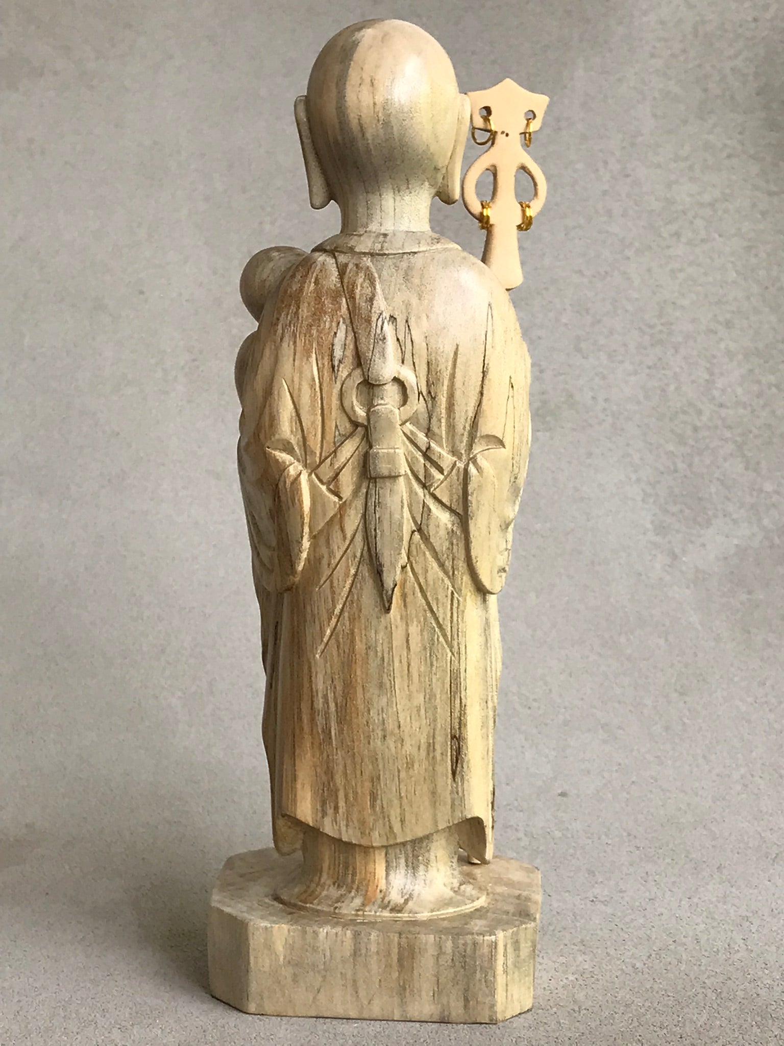 JIzo man standing, holding a staff and a baby, 25cm, 10 inches, color variation in wood from warm light brown to grey grain. back view.