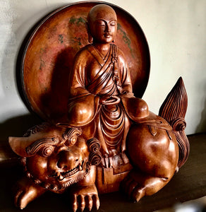 Woodcarving Manjushri as a young monk tranquilly seated in meditation on a lion with red lacquer tray behind