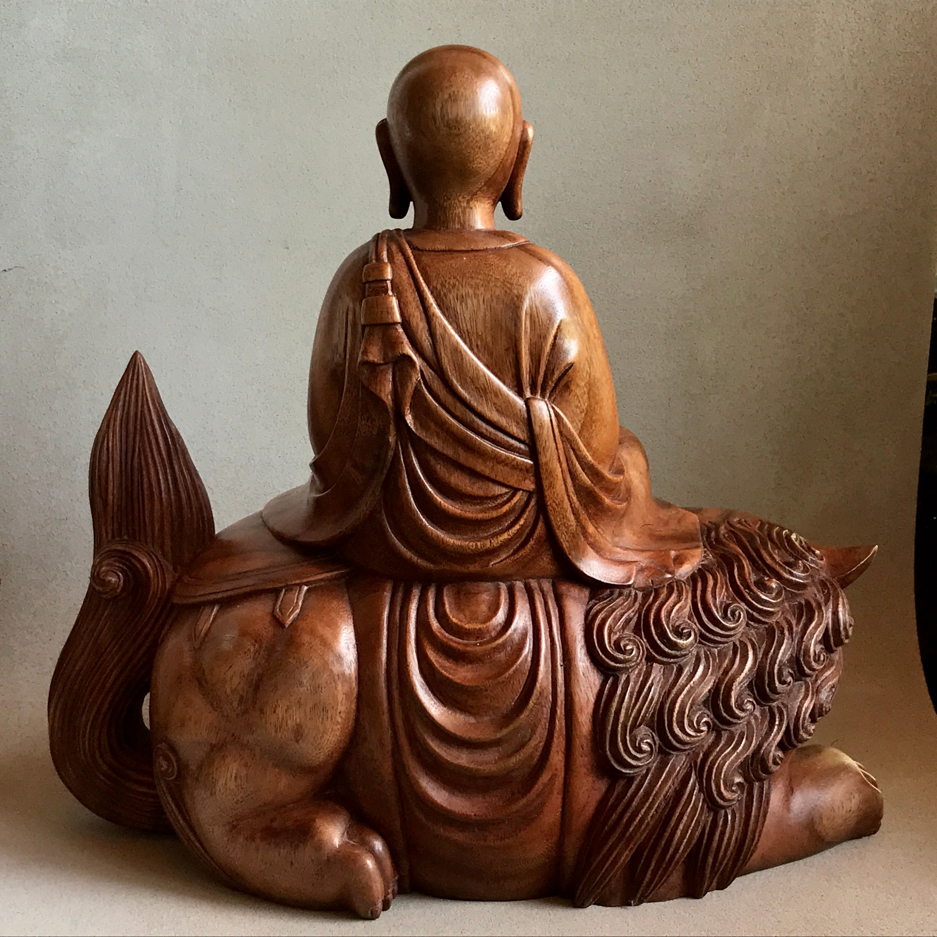 Woodcarving Manjushri as a young monk tranquilly seated in meditation on a lion back view beautiful curls in lions mane.