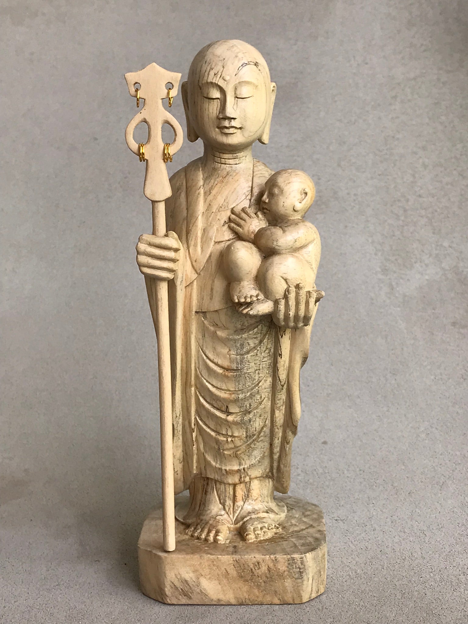JIzo man standing, holding a staff and a baby, 25cm, 10 inches, color variation in wood from warm light brown to grey grain.