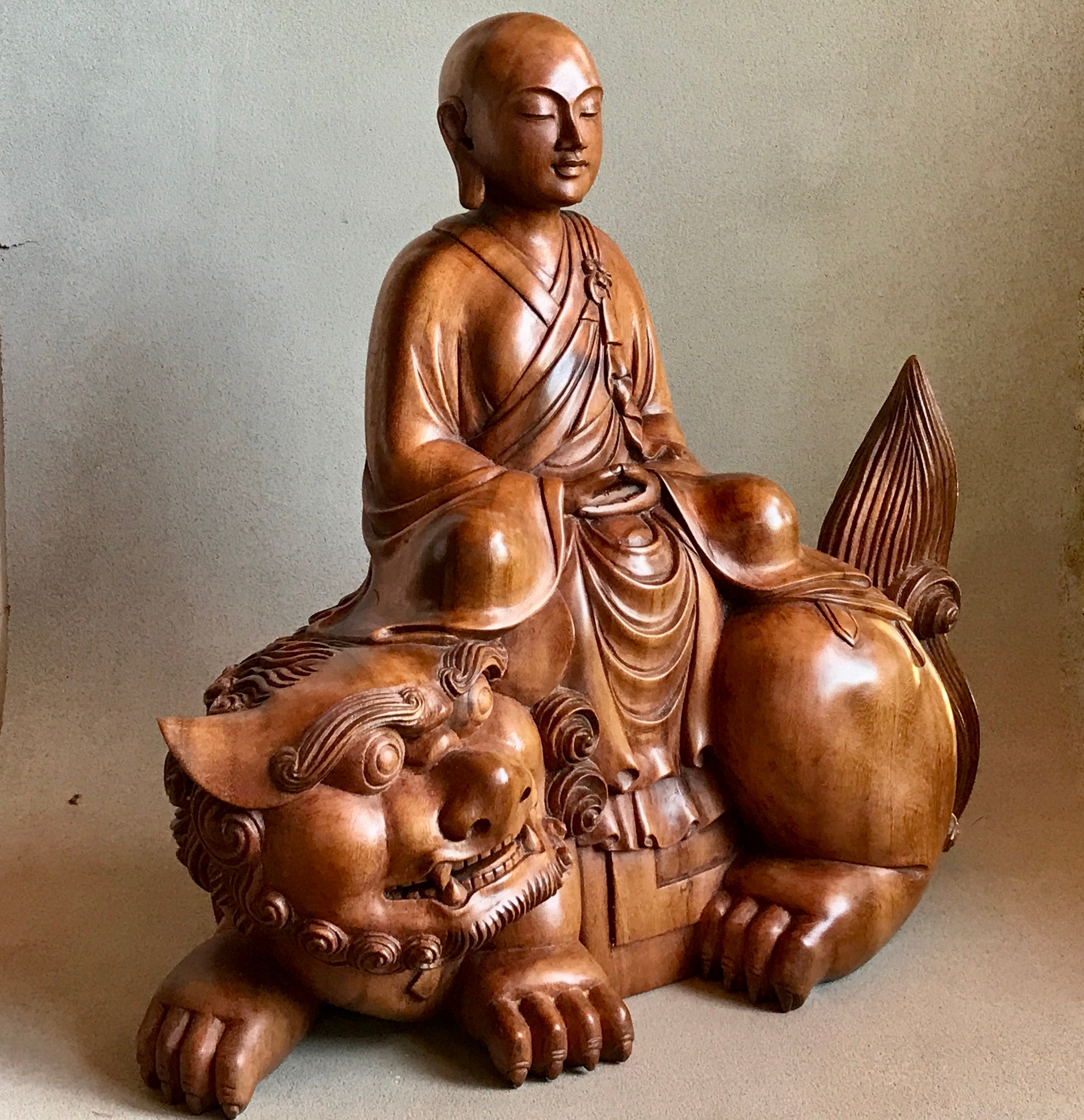 Woodcarving Manjushri as a young monk tranquilly seated in meditation on a lion.