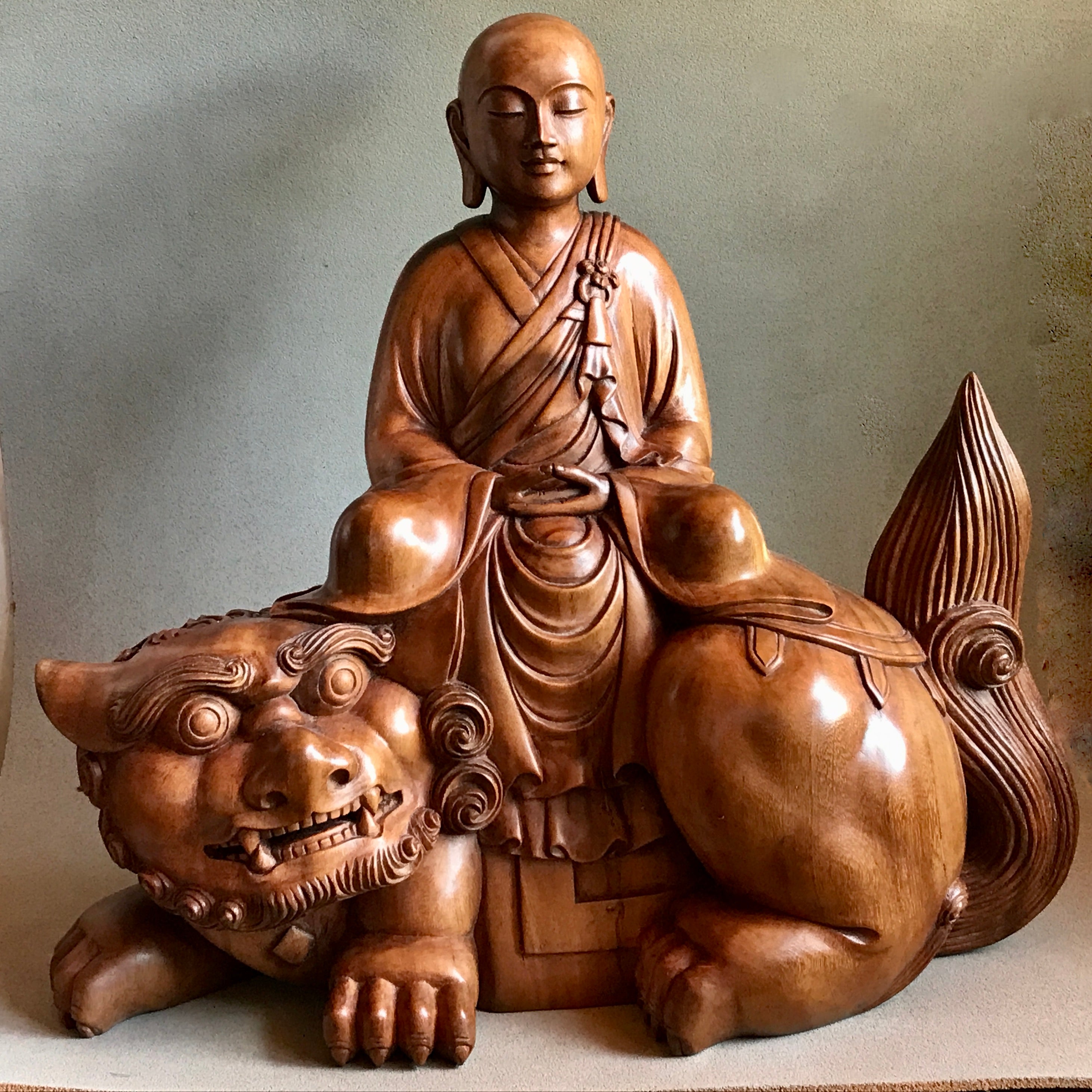 Woodcarving Manjushri as a young monk tranquilly seated in meditation on a lion.