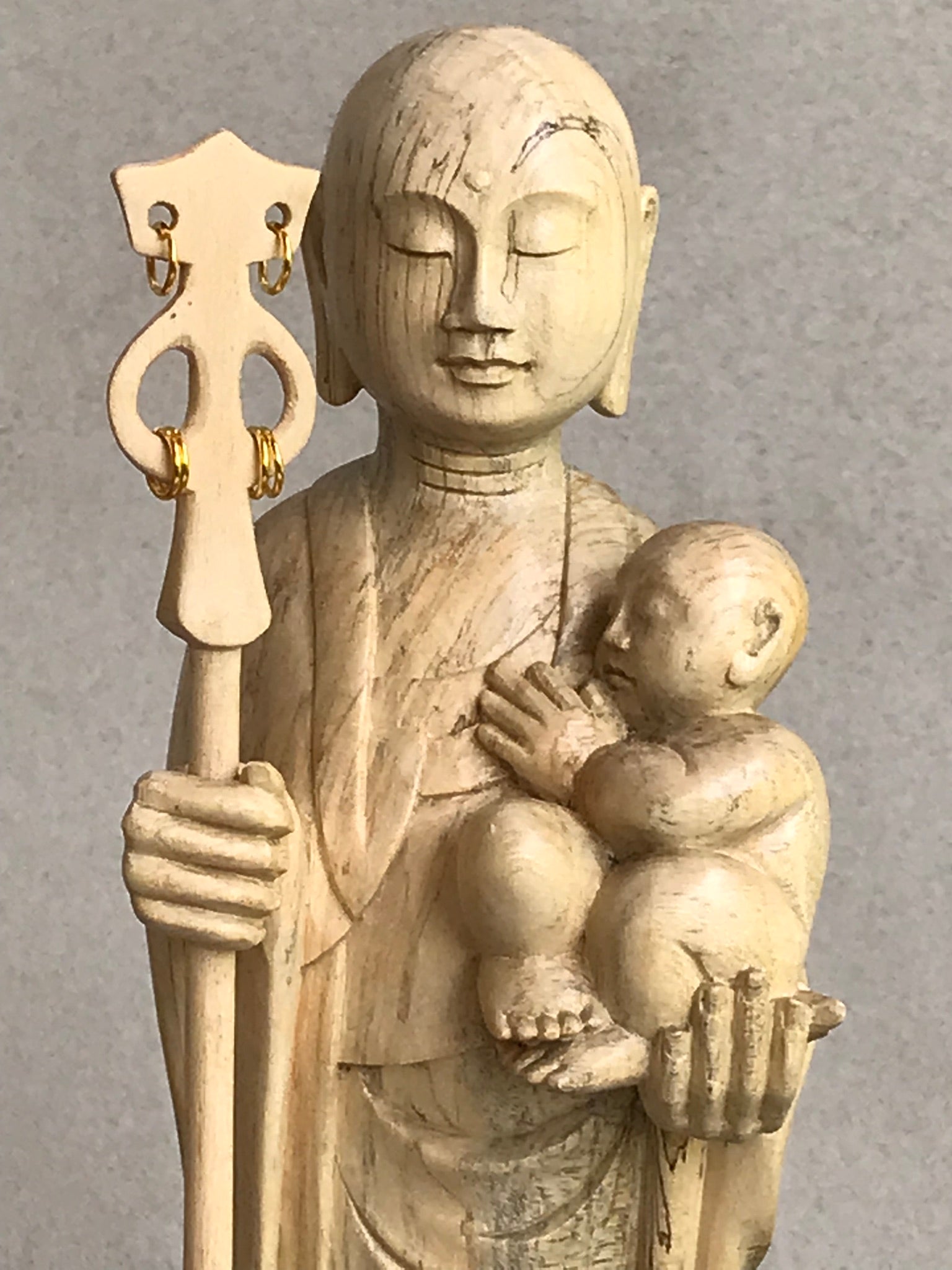 JIzo man holding a staff and a baby, 25cm, 10 inches, color variation in wood from warm light brownt to grey grain.