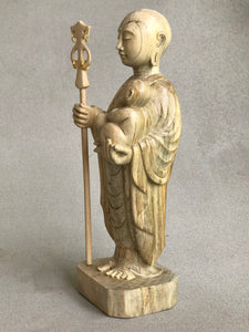 JIzo man standing, holding a staff and a baby, 25cm, 10 inches, color variation in wood from warm light brown to grey grain, 3/4 view.