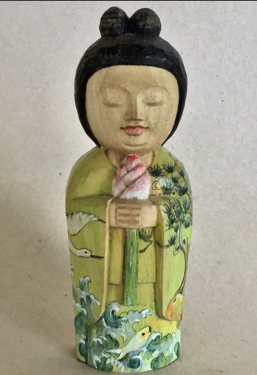 A little hand carved wood Kannon or Quan Yin. She has black hair with 2 top knots, natural light wood skin and her kimono is painted with cranes and fish and waves and pine trees. She is holding a lotus bud, which symbolizes our Buddha nature ready to be revealed.