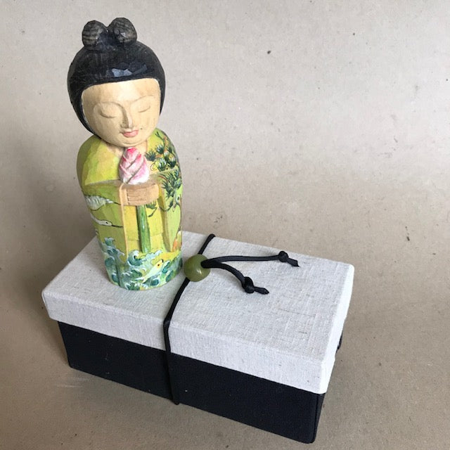 Little Japanese Woman statue called Kannon, the Bodhisattva of Compassion. Kimono painted with cranes, pines, waves and fish. Standing on her black gift box with white lid and cord with bead.